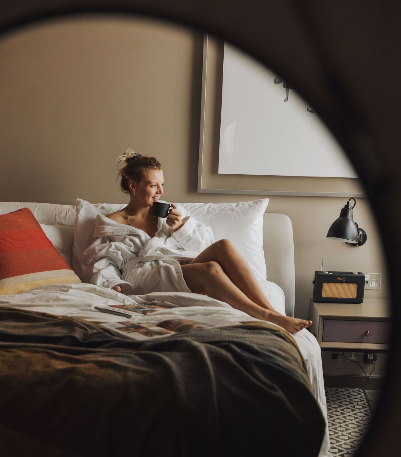 Woman in bathrobe relaxing on the bed and enjoying a beverage at The Londoner Hotel