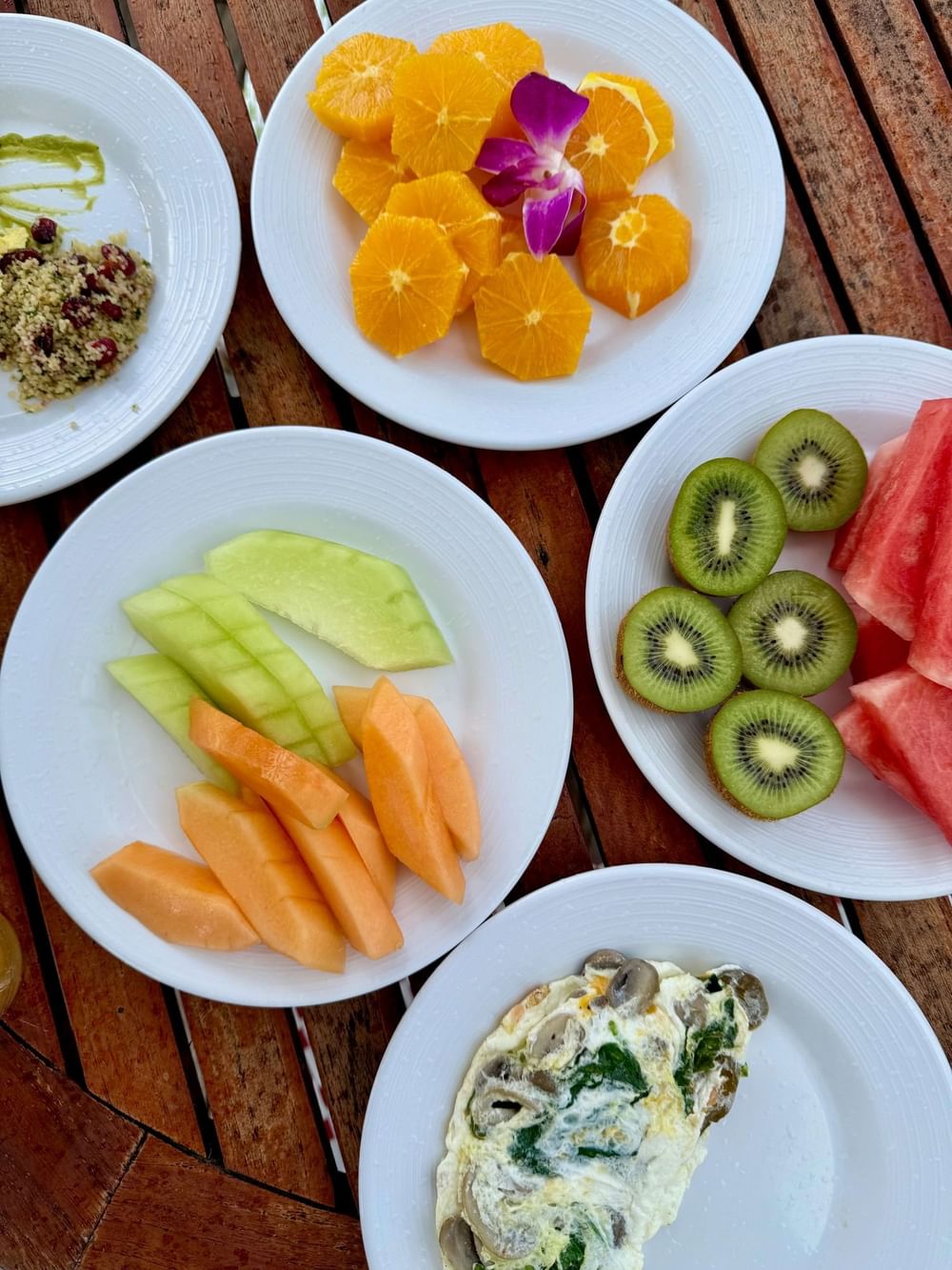 Five white plates with various fruits, an omelette, and garnishes on a wooden table at Warwick Hotels and Resorts