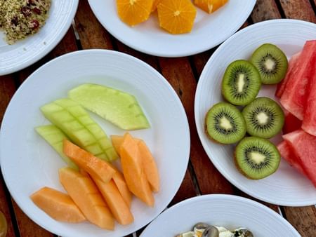 Five white plates with various fruits, an omelette, and garnishes on a wooden table at Warwick Hotels and Resorts