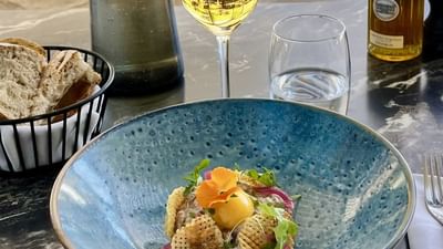 Bol bleu avec plat de poisson, verres, bouteilles et pain sur une table en marbre.