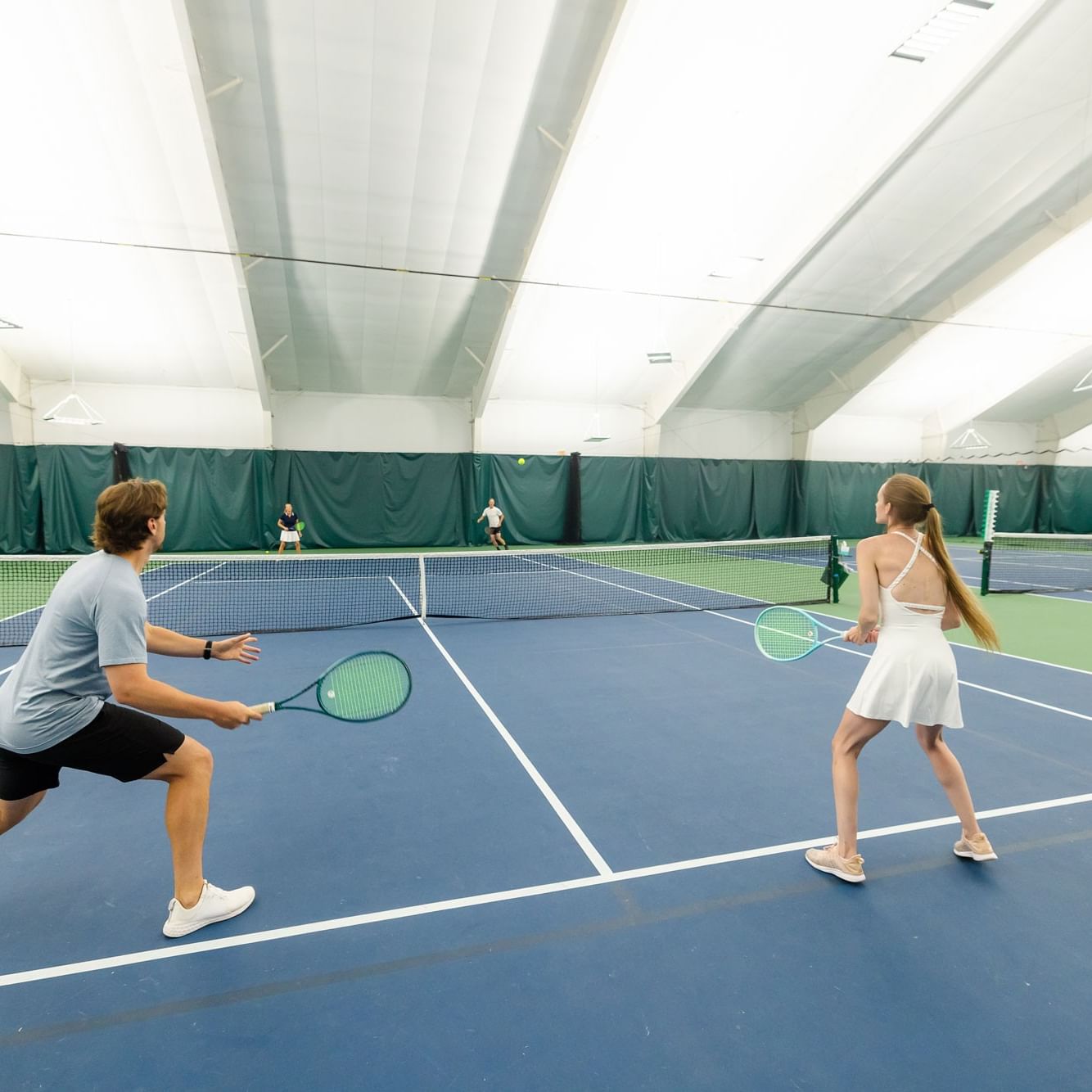 Man and woman playing mixed doubles round robin tennis on an indoor court.