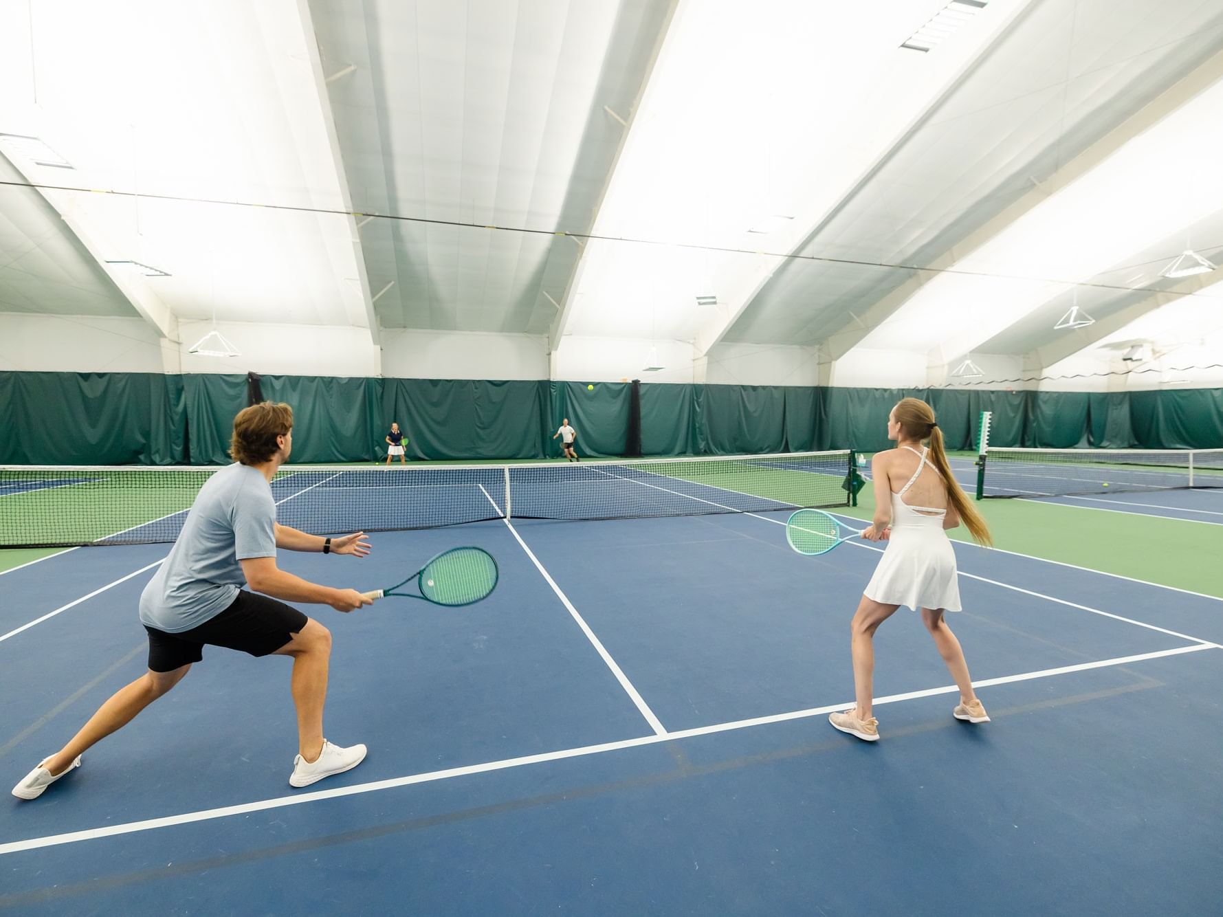 Man and woman playing mixed doubles round robin tennis on an indoor court.