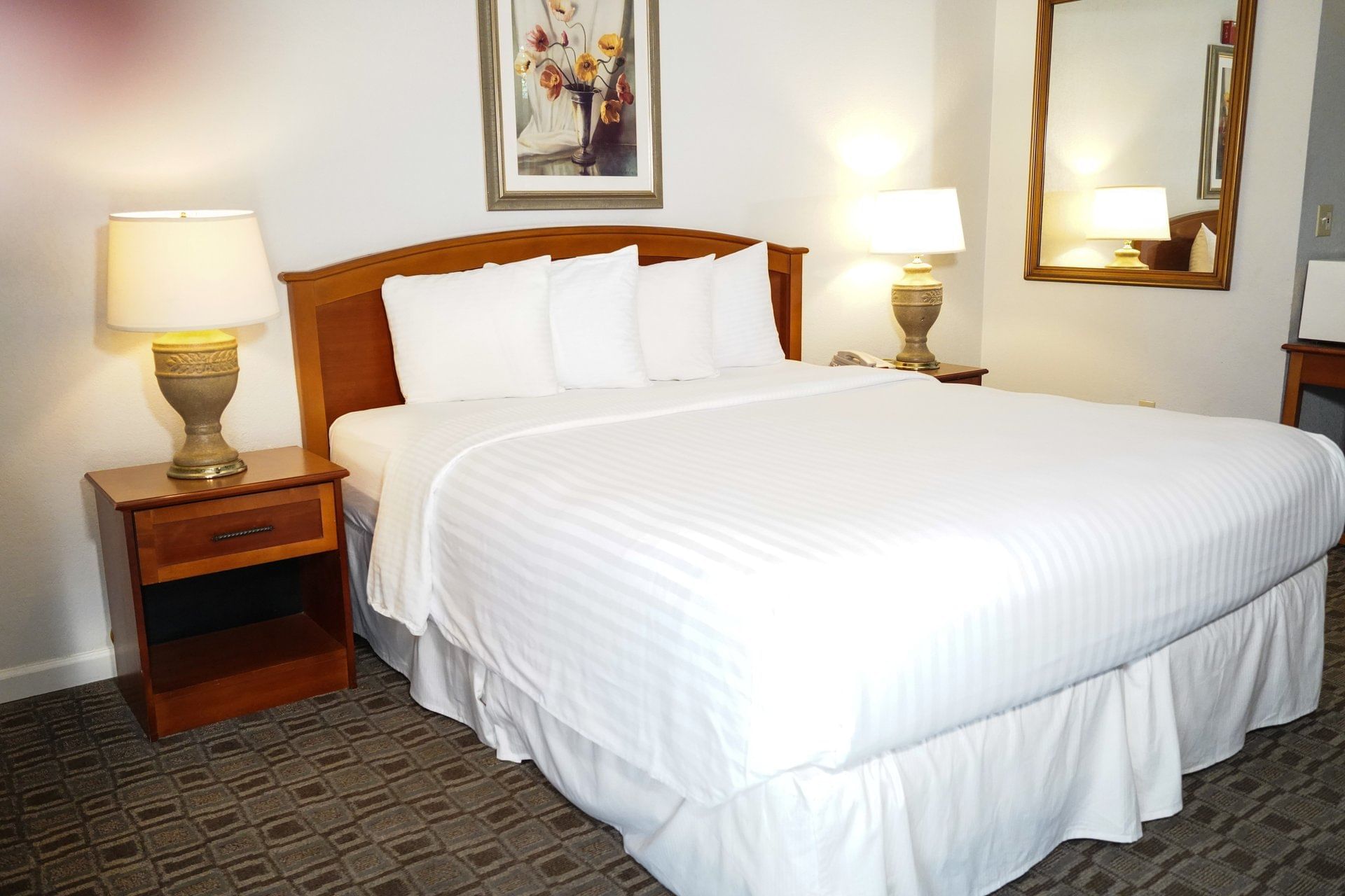 A hotel room with a large bed, two nightstands, and a mirror