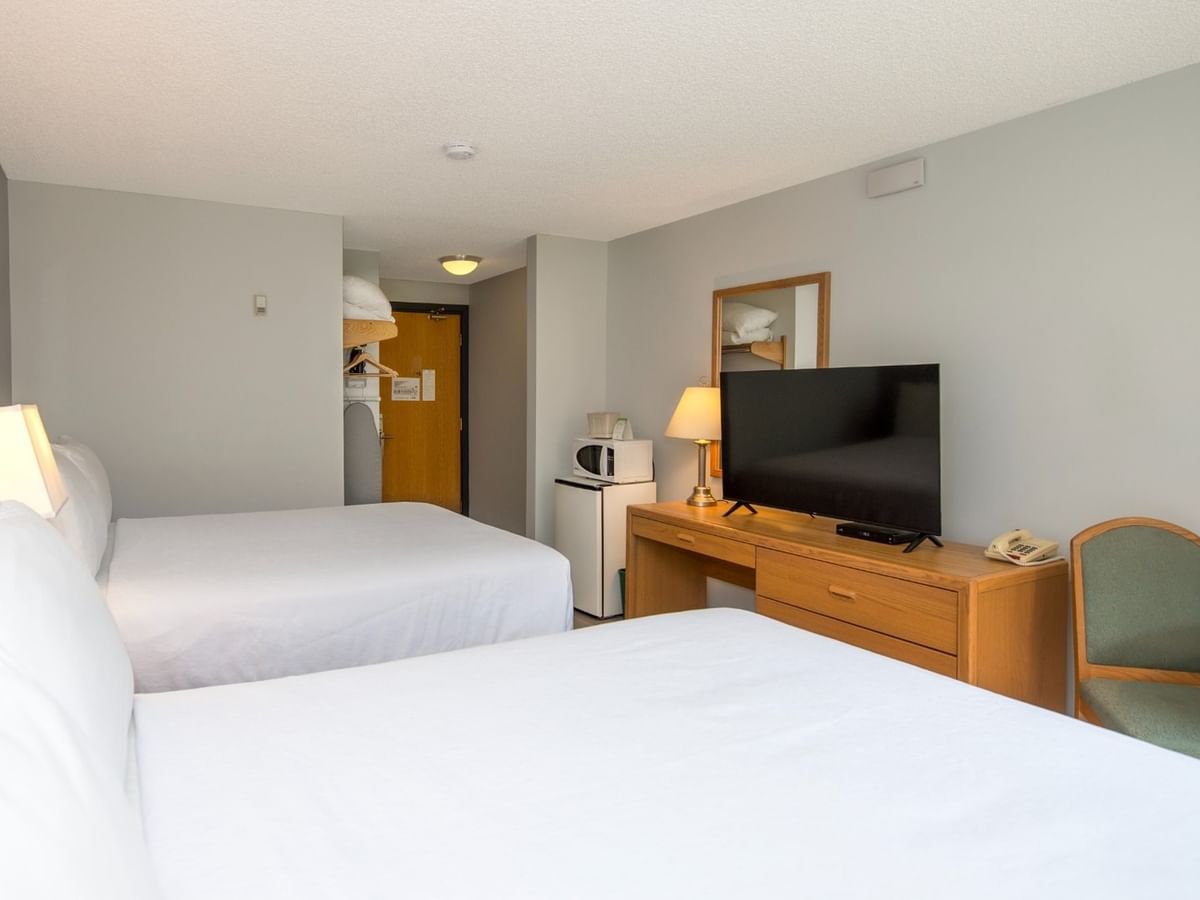 A hotel room with two beds, a desk, a TV, a microwave, and a chair.