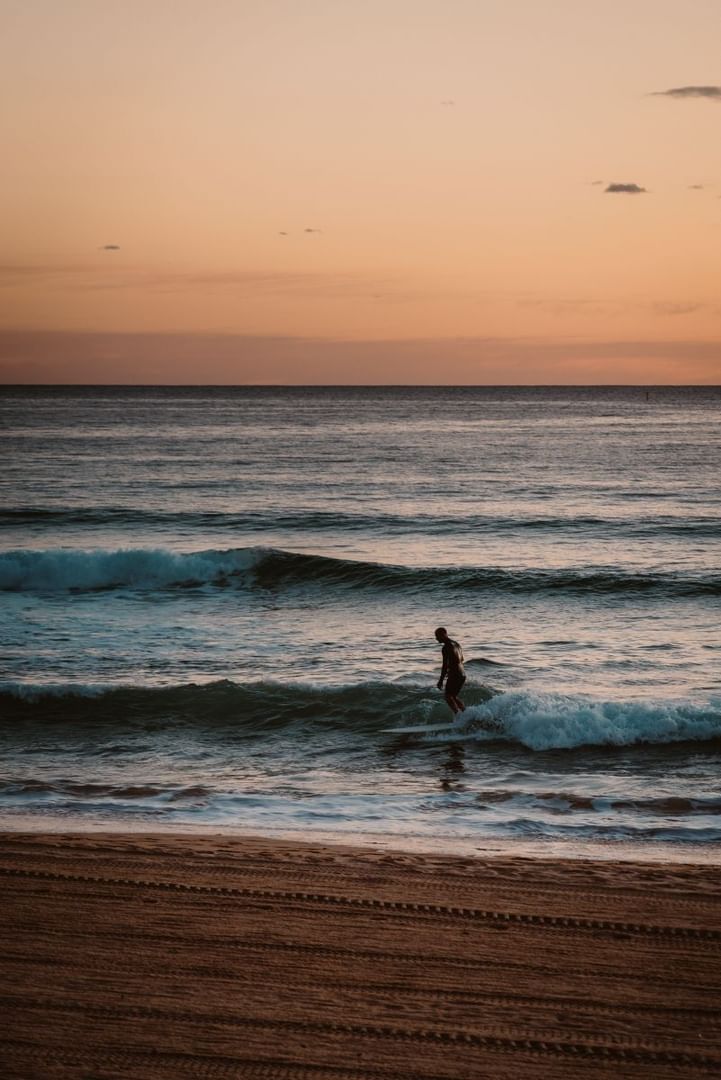 Sunset beach view at Elysium Manly featuring the silhouette of a lone surfer, highlighting things to do at Manly