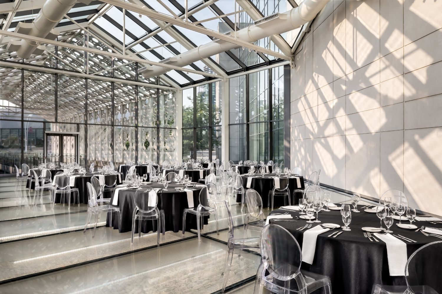 Glass greenhouse venue with clear ghost chairs around banquet tables set for a formal dinner at Hotel X Toronto