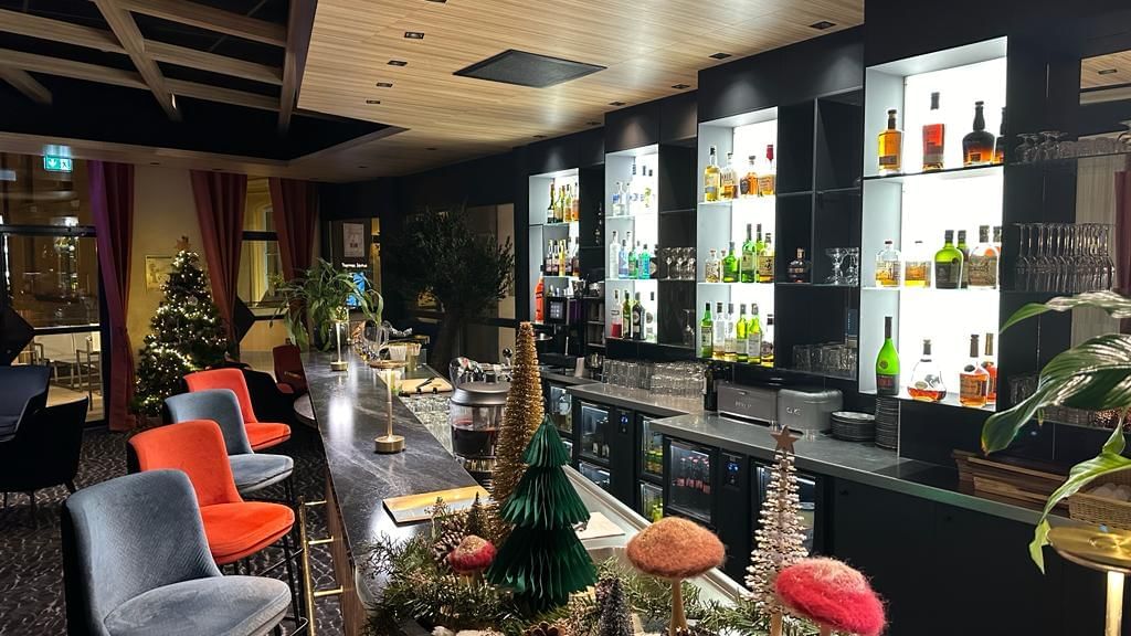 Bar avec des étagères bien garnies de bouteilles d'alcool, des décorations de Noël et des chaises confortables.