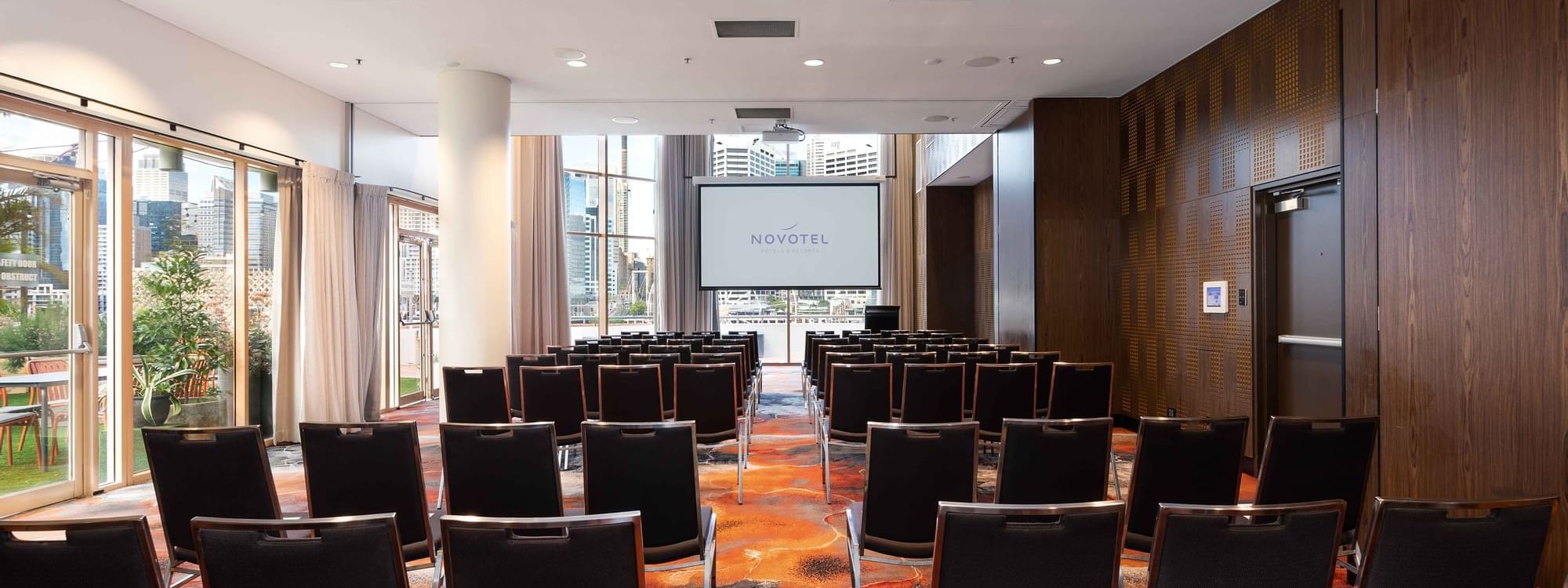 Theater style table set-up facing the projector screen in The Hunter Room 1-3 at Novotel Sydney on Darling Harbour