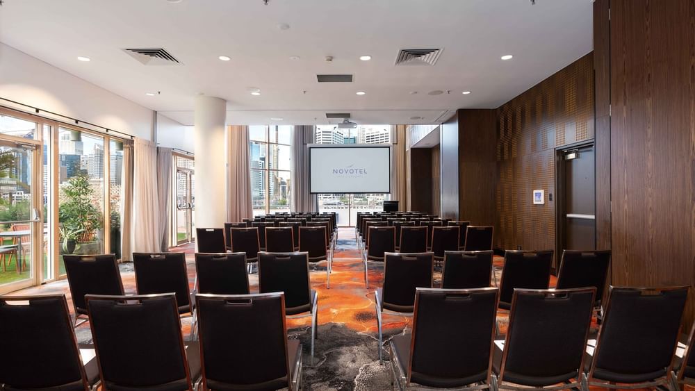 Theater style table set-up facing the projector screen in The Hunter Room 1-3 at Novotel Sydney on Darling Harbour