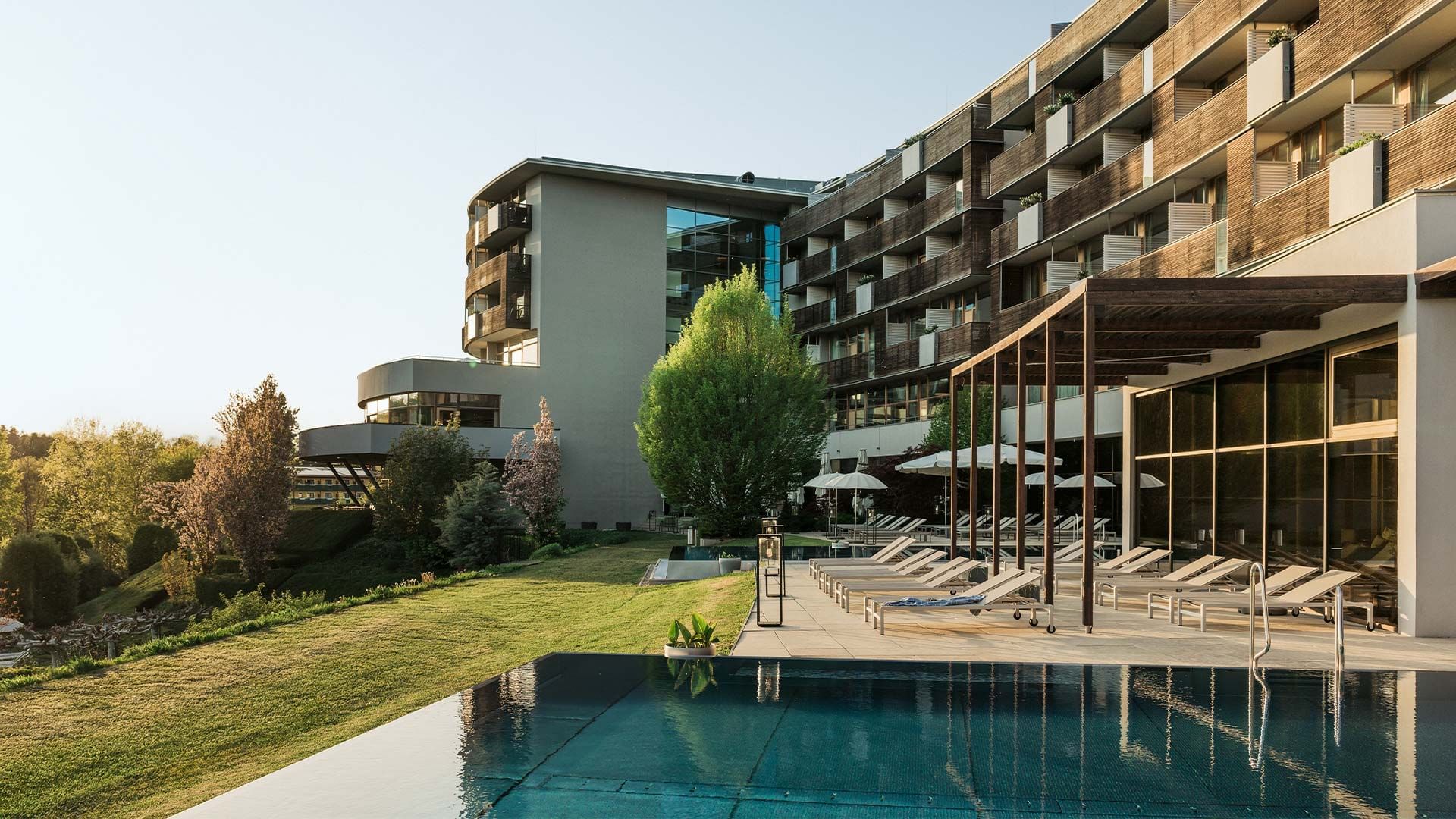 Piscina esterna con lettini di un resort di lusso con architettura moderna e ampio prato verde.