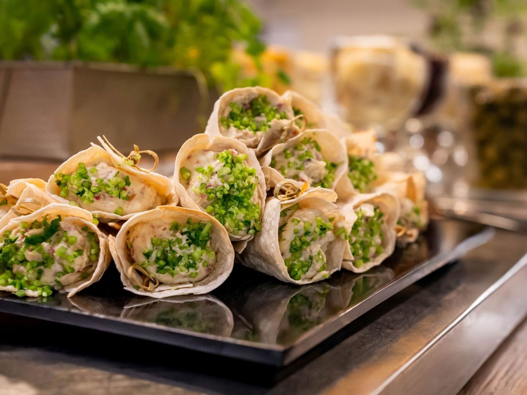 Plato de rollitos de comida envueltos con guarnición verde por encima en un bufé.
