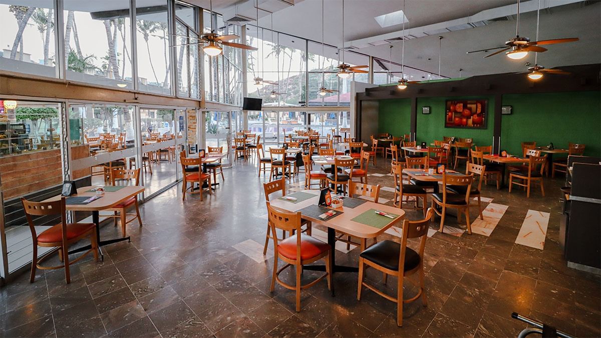 Amplio comedor con mesas de madera y grandes ventanales en La Pérgola, dentro de Araiza Palmira 