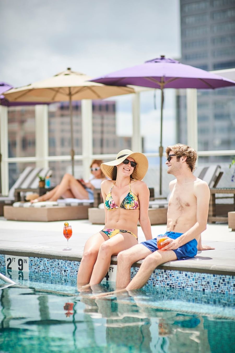 Couple by a pool under a sun hat near striped lounge chairs and drinks at Warwick Denver