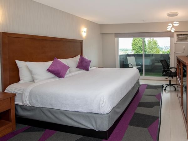 Hotel room with a large bed, purple pillows, wooden furniture, and a balcony.