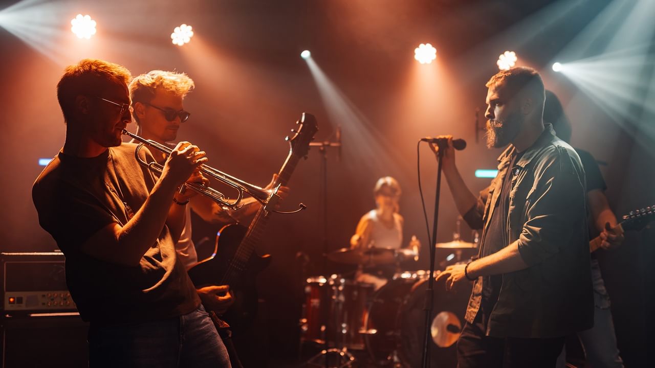 Live band performing on stage with trumpet player, guitarist, vocalist, and drummer under dramatic stage lighting