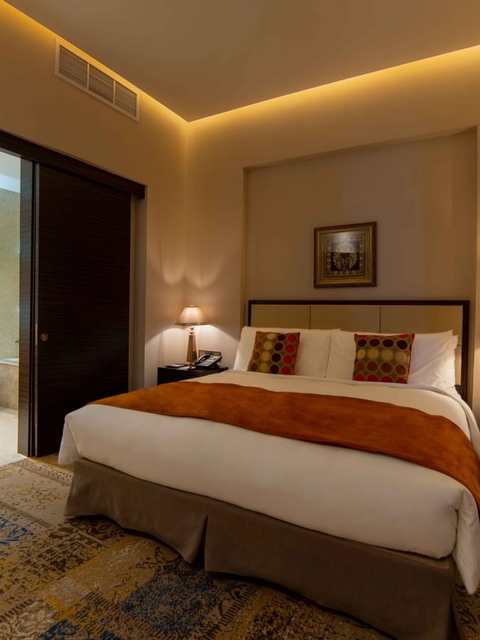 King bed with an orange runner by lamps under warm recessed lighting in Executive Room at Warwick Al Khobar