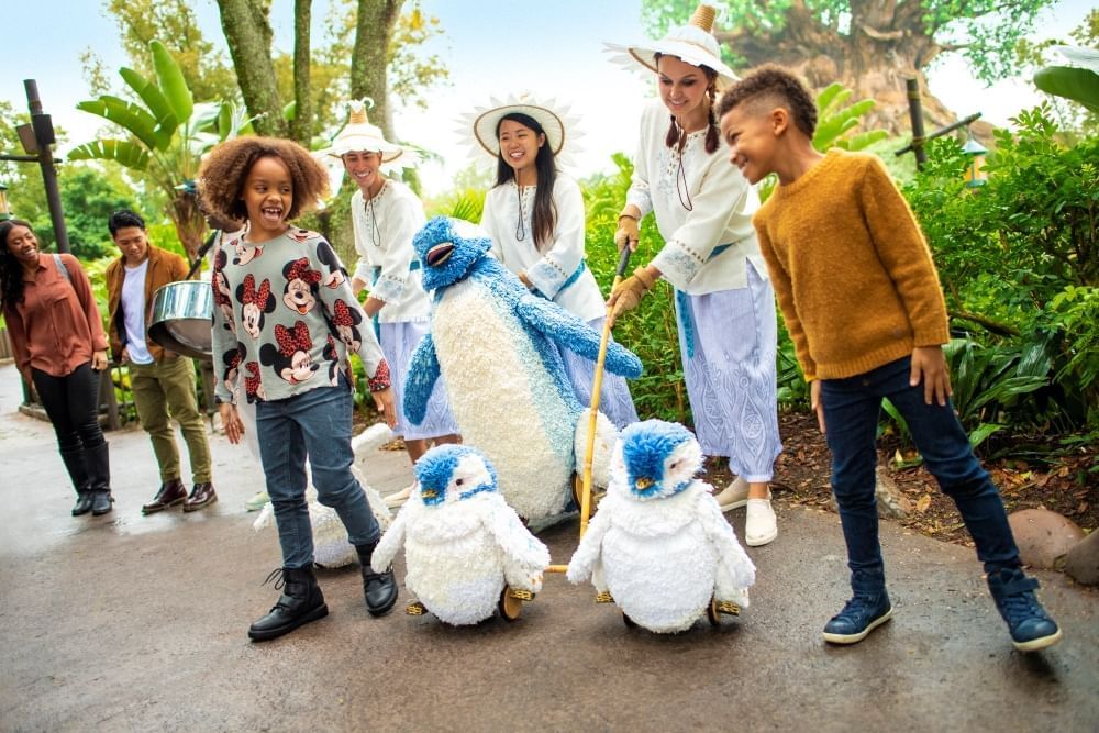 Two children dance with blue and white penguin puppets and puppeteers in Animal Kingdom.