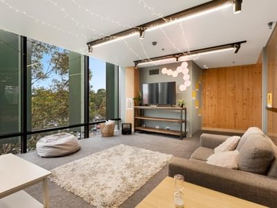 Modern apartment lounge with large windows, cozy couches, and a flat-screen TV.