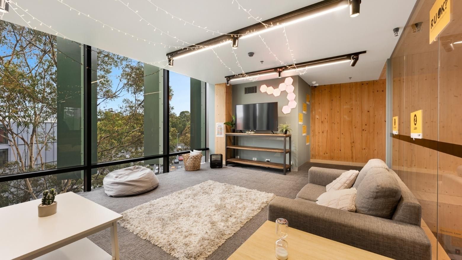 Modern apartment lounge with large windows, cozy couches, and a flat-screen TV.