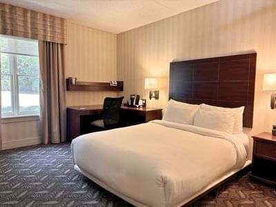 Bed beside a dark wood work desk and a rolling office chair inside the guest room at Spencer Hotel & Conference Centre