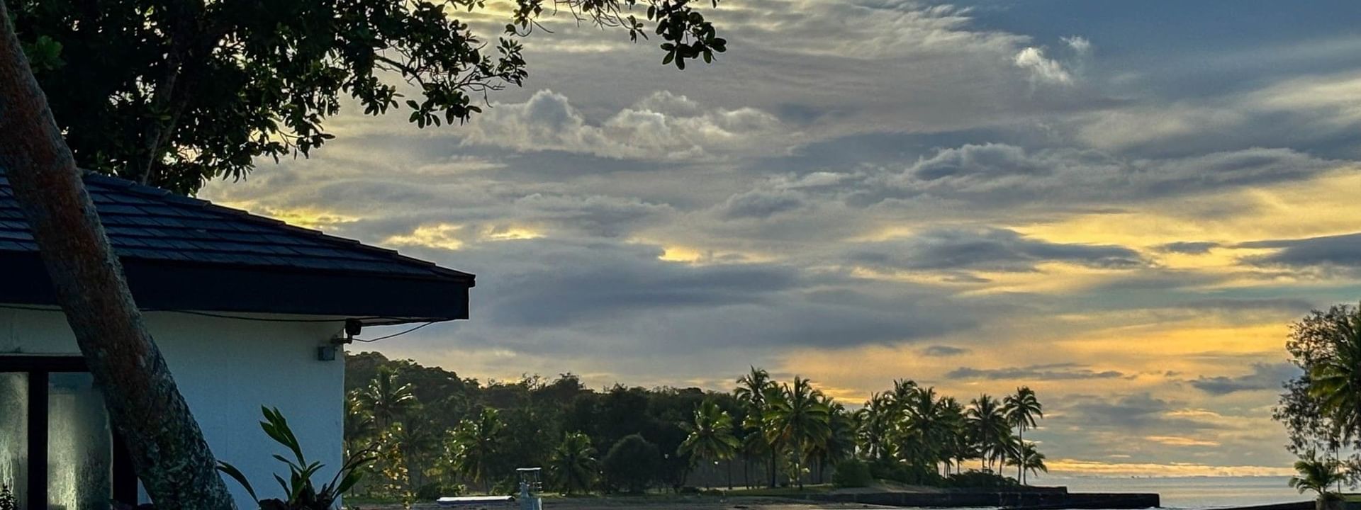 Sunset view over water with boats near tropical trees and a building at The Naviti Resort in Korolevu
