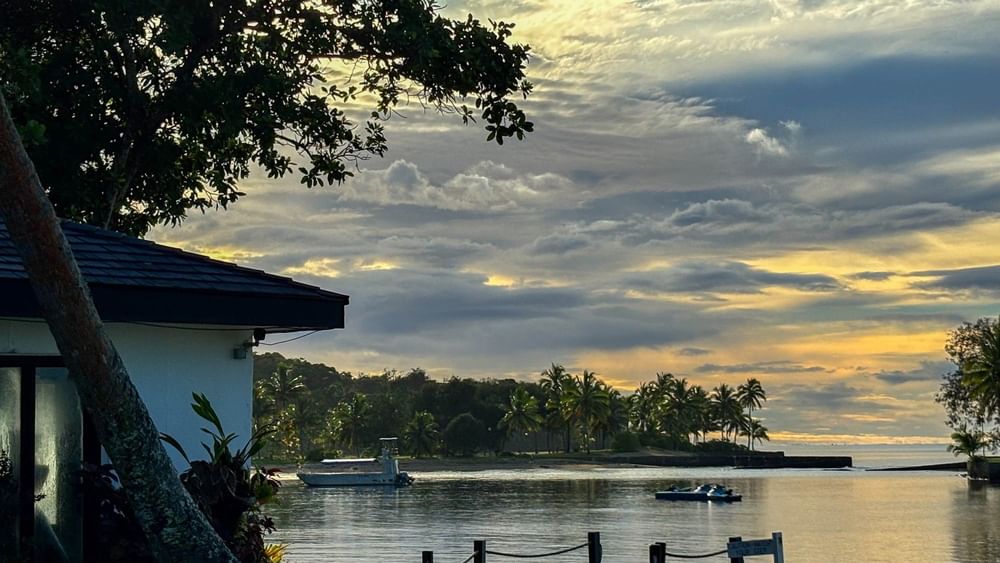 Sunset view over water with boats near tropical trees and a building at The Naviti Resort in Korolevu.