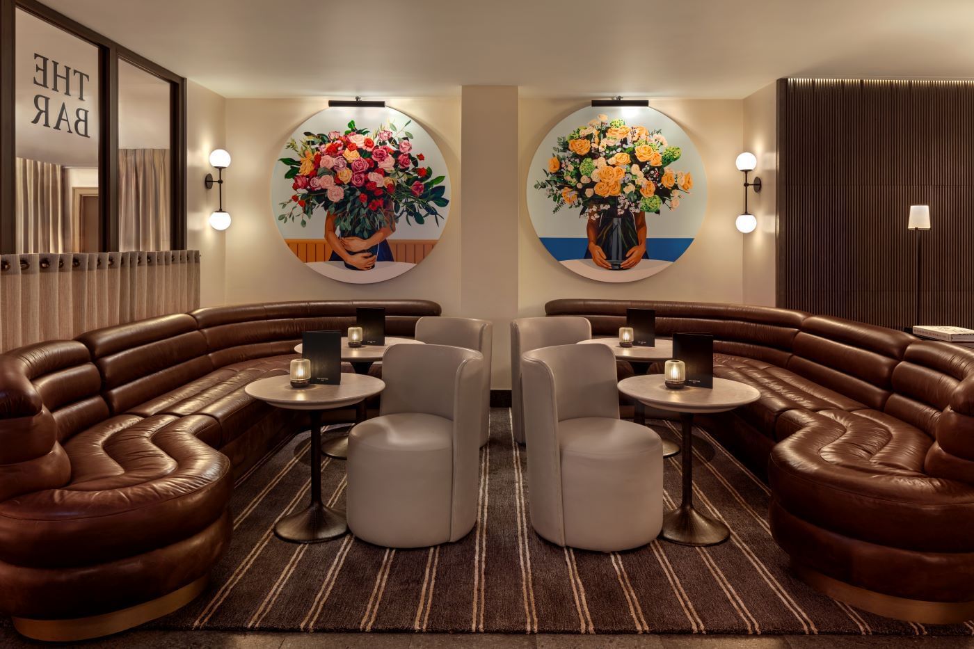 Brown couch seating with round tables and floral wall art in a The May Fair Bar