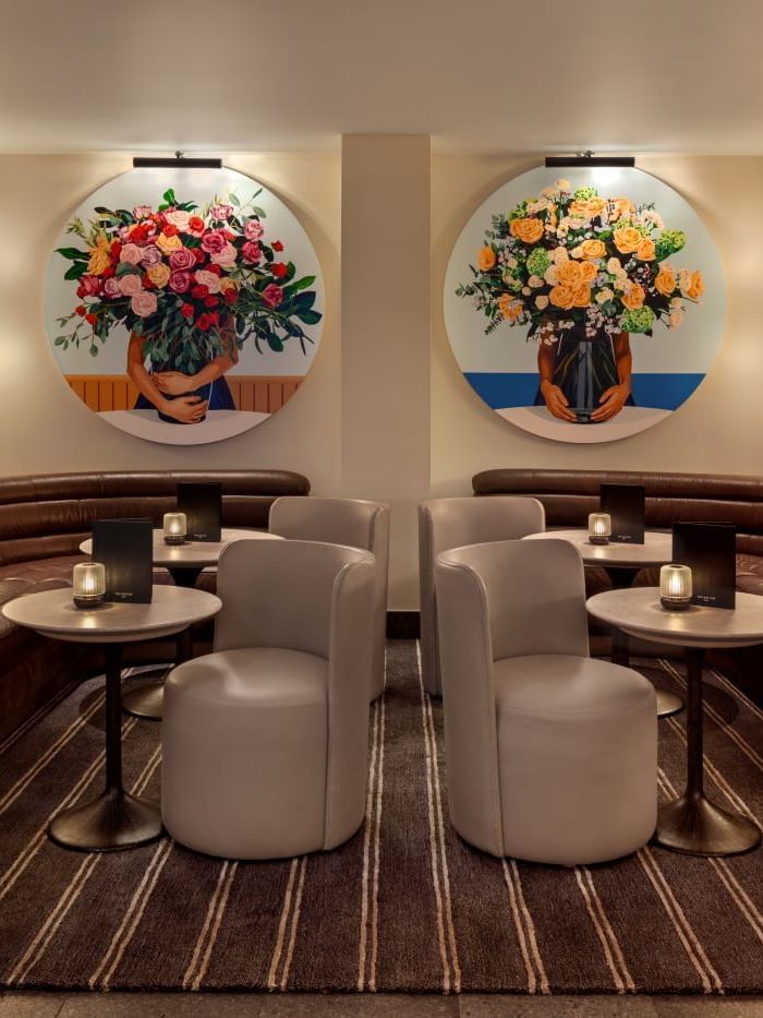 Brown couch seating with round tables and floral wall art in a The May Fair Bar