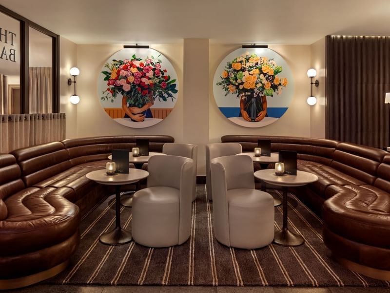 Brown couch seating with round tables and floral wall art in a The May Fair Bar