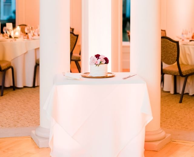 Small floral-topped cake on a table between white columns, with set dining tables at Mountain View Grand Resort & Spa
