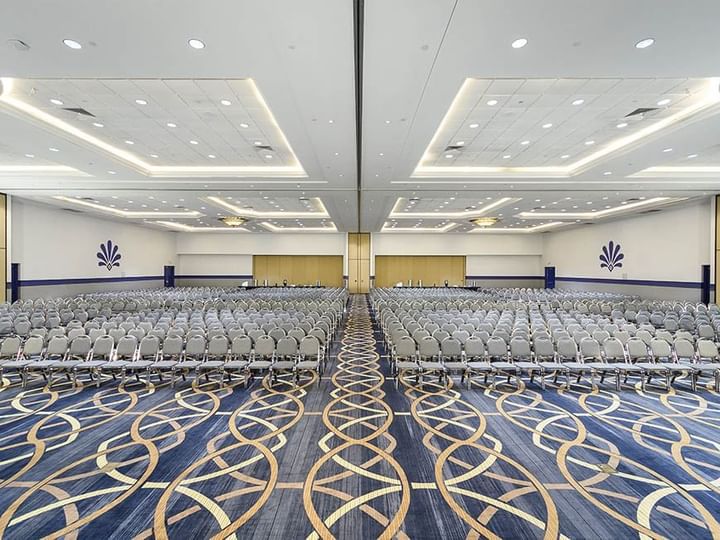 A large meeting room with rows of gray chairs, blue and gold carpet, and white walls.