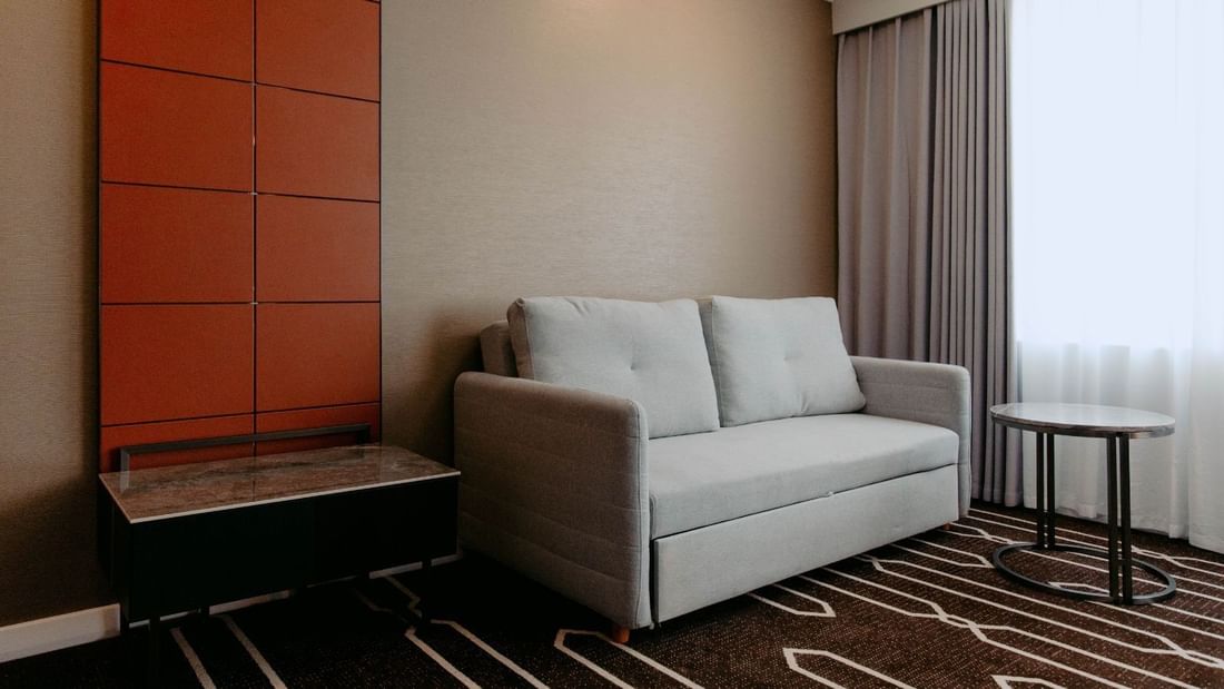 Living room with gray couch, round table, and orange paneled wall next to window with curtains.