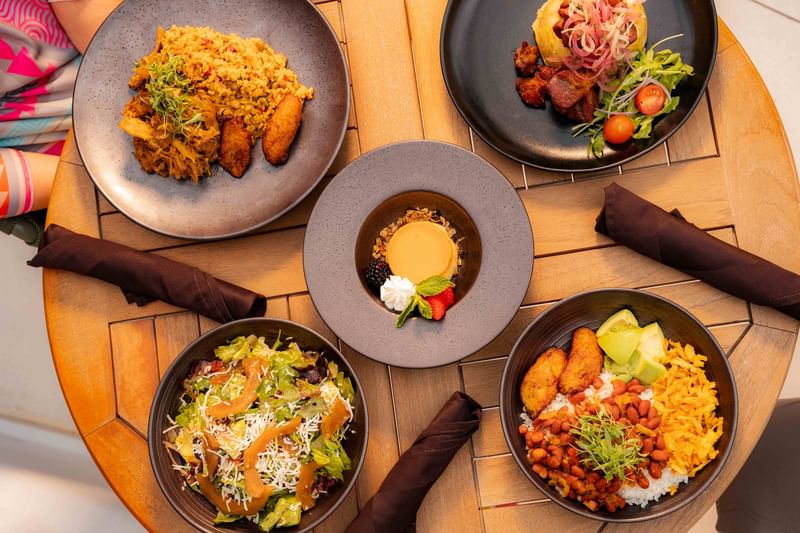Top view of a round wooden table featuring a spread of traditional dishes and a flan dessert at El Conquistador Resort