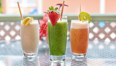 Three colorful glasses of fresh smoothies with straws and fruit garnishes on a table at Worthing Court Apartment