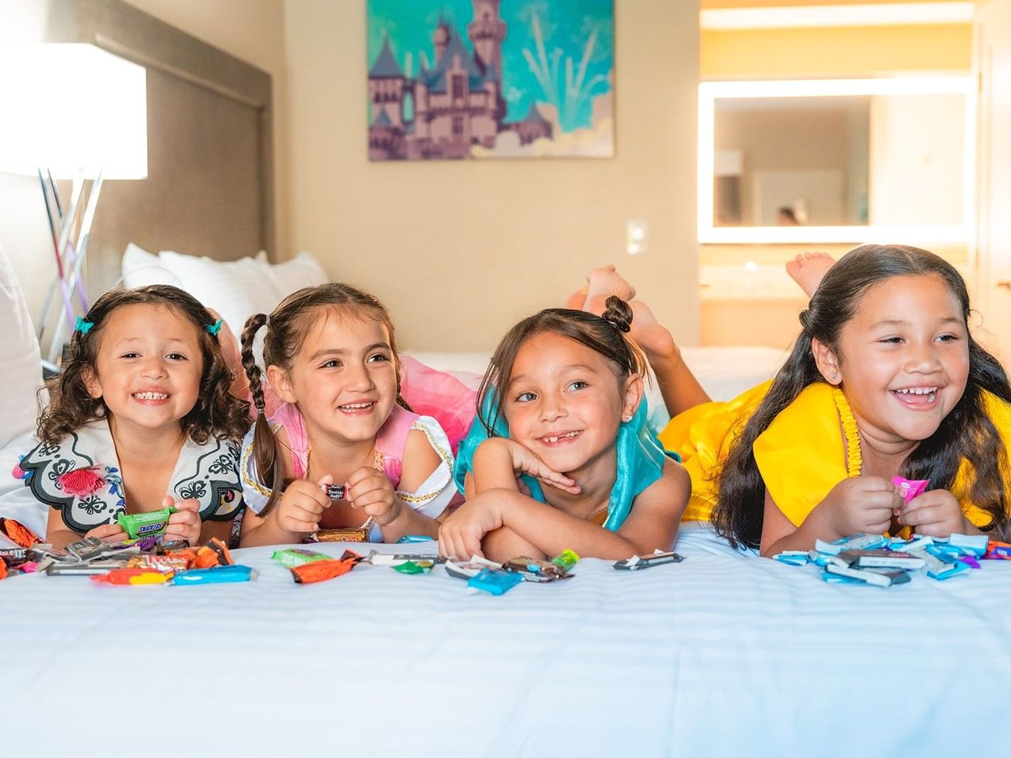 4 little girls in Halloween costume on a hotel bed with candy