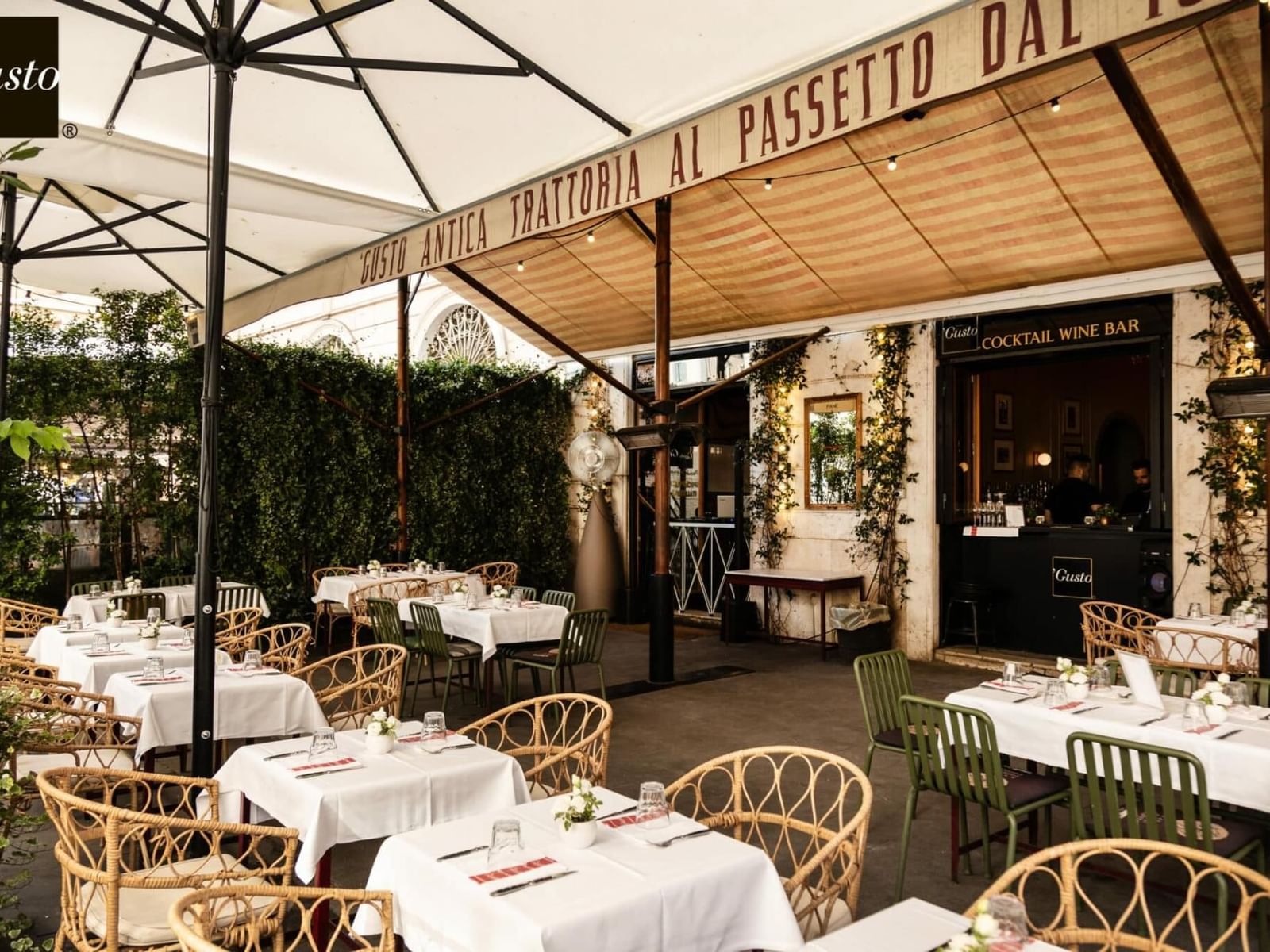 Charming Gusto outdoor dining near The Guardian Hotel with white tablecloths, rattan chairs, a canopy, and lush greenery
