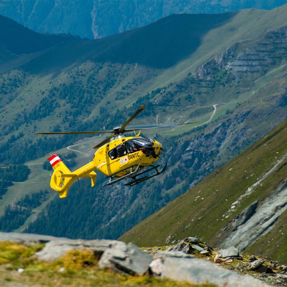 Yellow rescue helicopter flying over mountainous terrain during 5th Mountain Rescuer Fantasy Day.