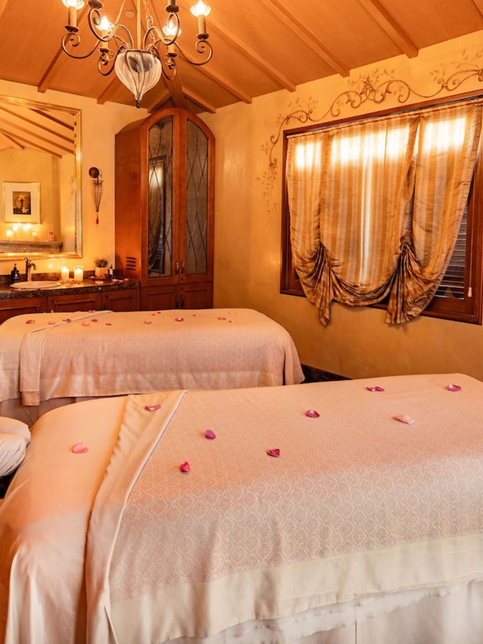 Elegant spa treatment room featuring two massage beds, a chandelier, and warm, classic wooden decor at Kelly's Spa