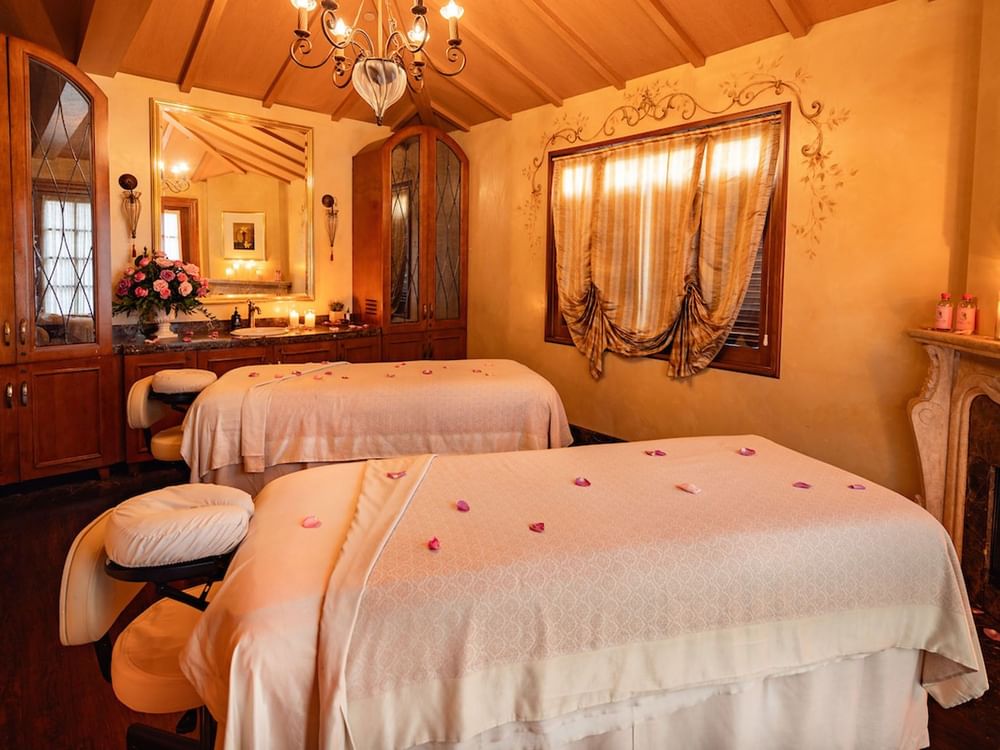 Elegant spa treatment room featuring two massage beds, a chandelier, and warm, classic wooden decor at Kelly's Spa