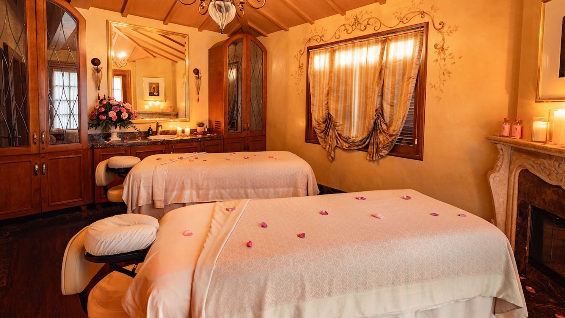 Elegant spa treatment room featuring two massage beds, a chandelier, and warm, classic wooden decor at Kelly's Spa