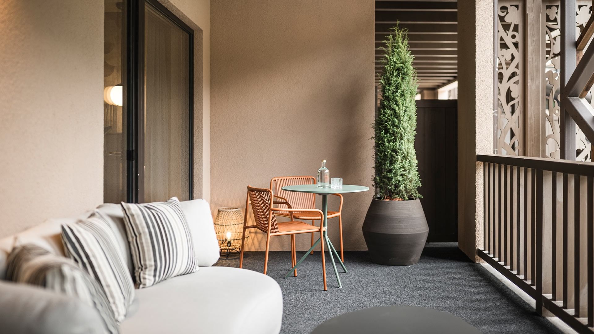 Balkon mit Tisch, Stühlen, großer Pflanze und Couch mit gestreiften Kissen.