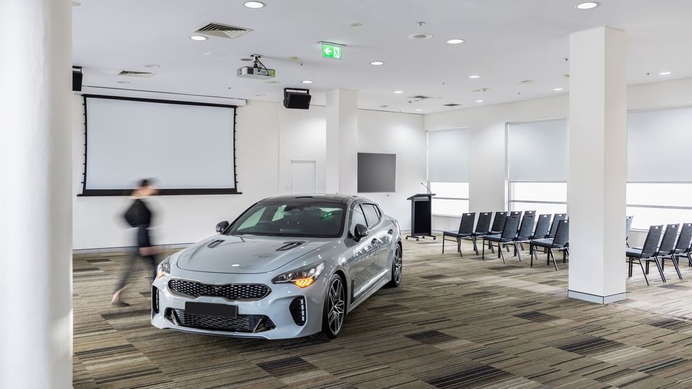 Car parked in Parklands Room with a blurred figure walking past and a nearby theatre set-up at Novotel Sydney Olympic Park