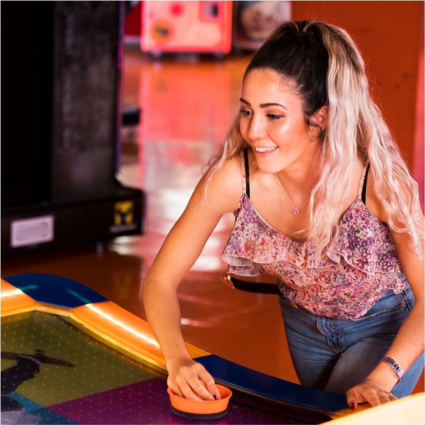 Mujer sonriente se inclina sobre una mesa de hockey de aire con un mazo naranja en el arcade de Megapolis Hotel Panama