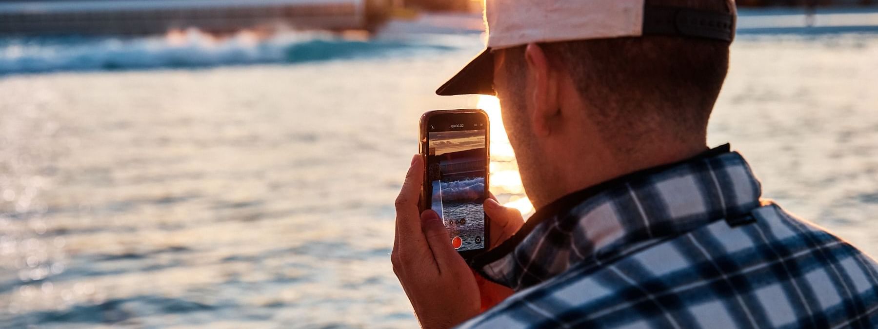 Man capturing a seaside sunset on their smartphone at URBNSURF Sydney near Novotel Sydney Olympic Park