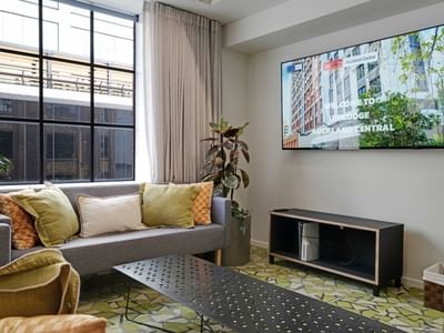 Modern living room with gray sofa, yellow cushions, large windows, and wall-mounted TV at UniLodge Auckland Central