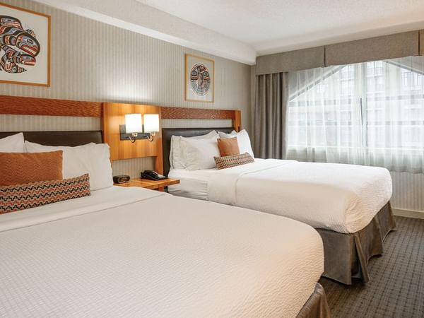 Spacious hotel room with two queen beds, elegant decor and large window for natural light.