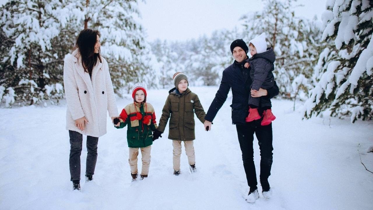Family of four in winter clothing standing in snow, with two adults holding hands of two children.