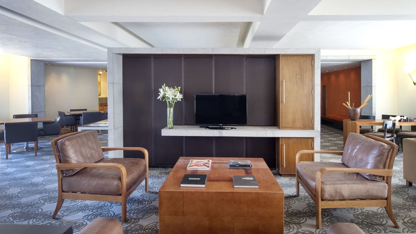 Modern lobby with brown leather chairs and a coffee table facing a TV at Grand Fiesta Americana
