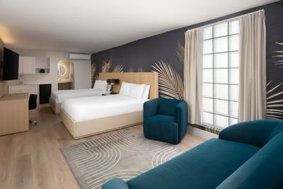 Premium Mini Suite Two Queens with two beds, a dark leaf mural, and a blue armchair at The Harrison Hotel Downtown Hollywood