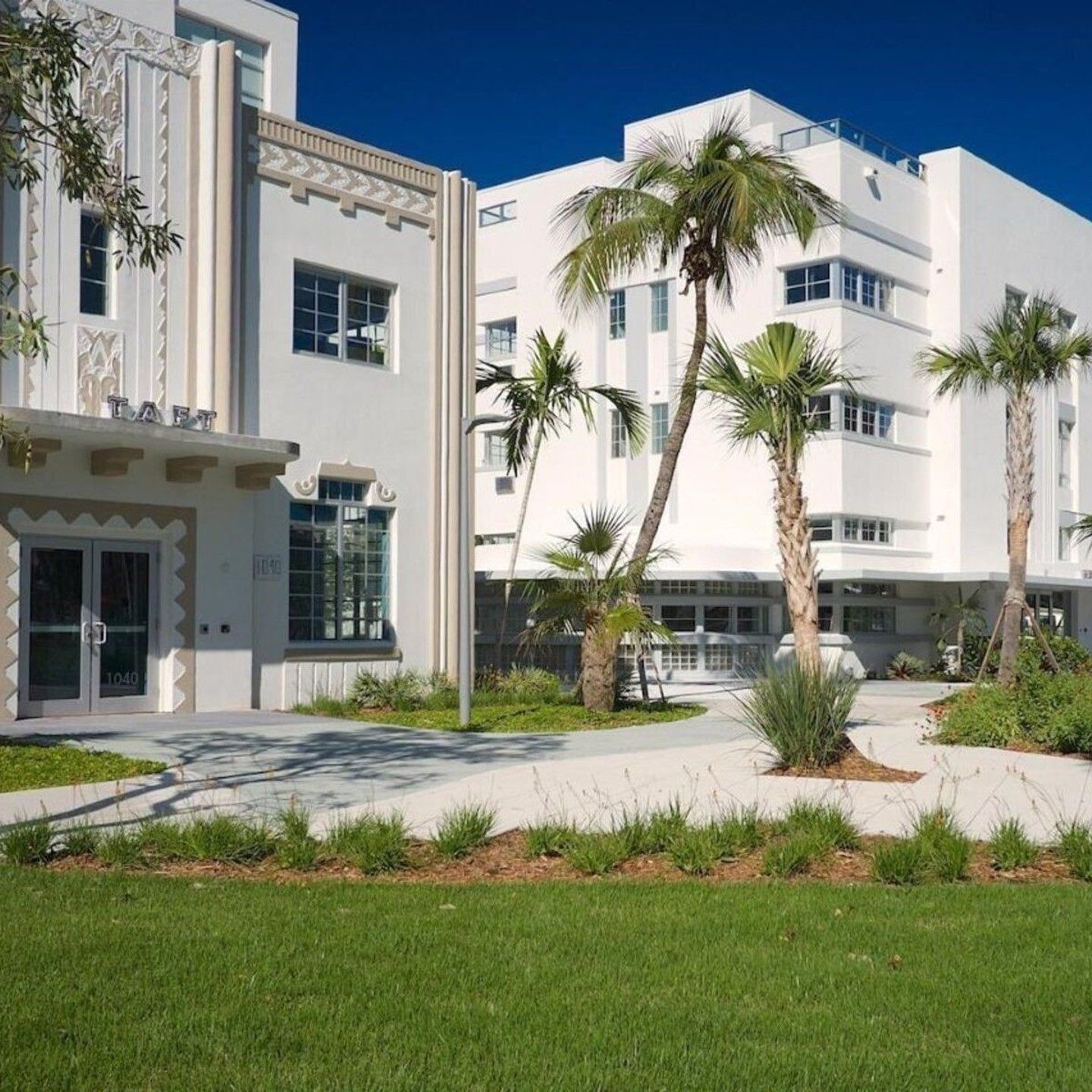 White Art Deco-style building with palm trees and landscaped grounds under a clear blue sky in South Beach Miami